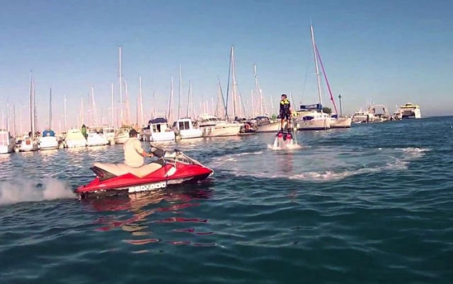 hombre volando en el aire mientras practica flyboard con varios barcos de fondo.jpg